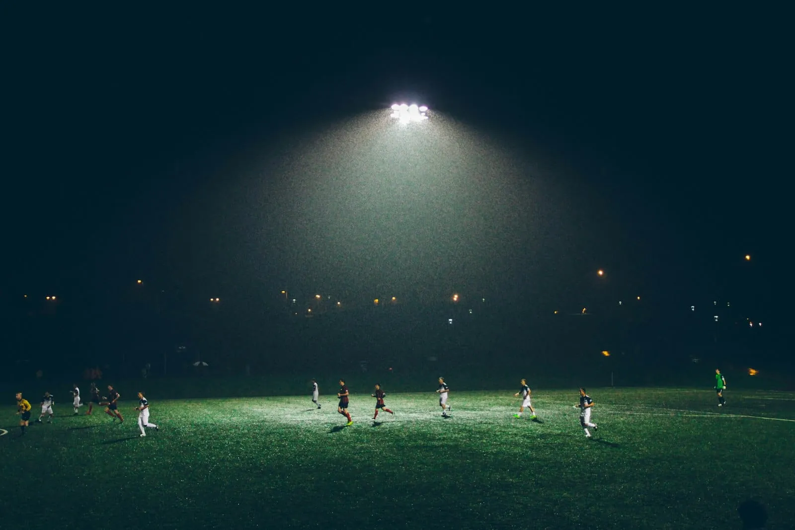 Floodlit night soccer match in the rain, players in motion under stadium lights in Northern BC