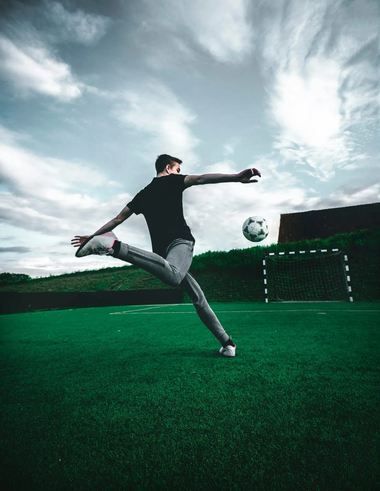 Youth player executing a freestyle kick, low-angle frame against a dramatic sky